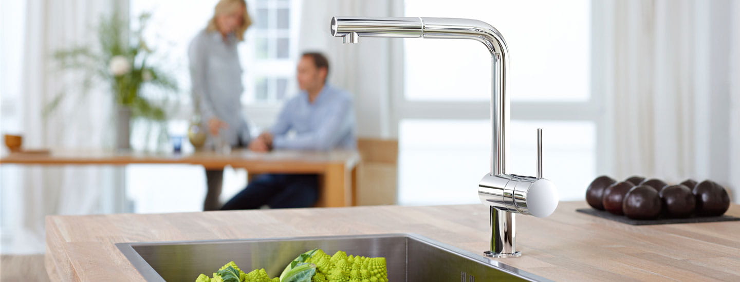 kitchen faucet with two people out of focus in background