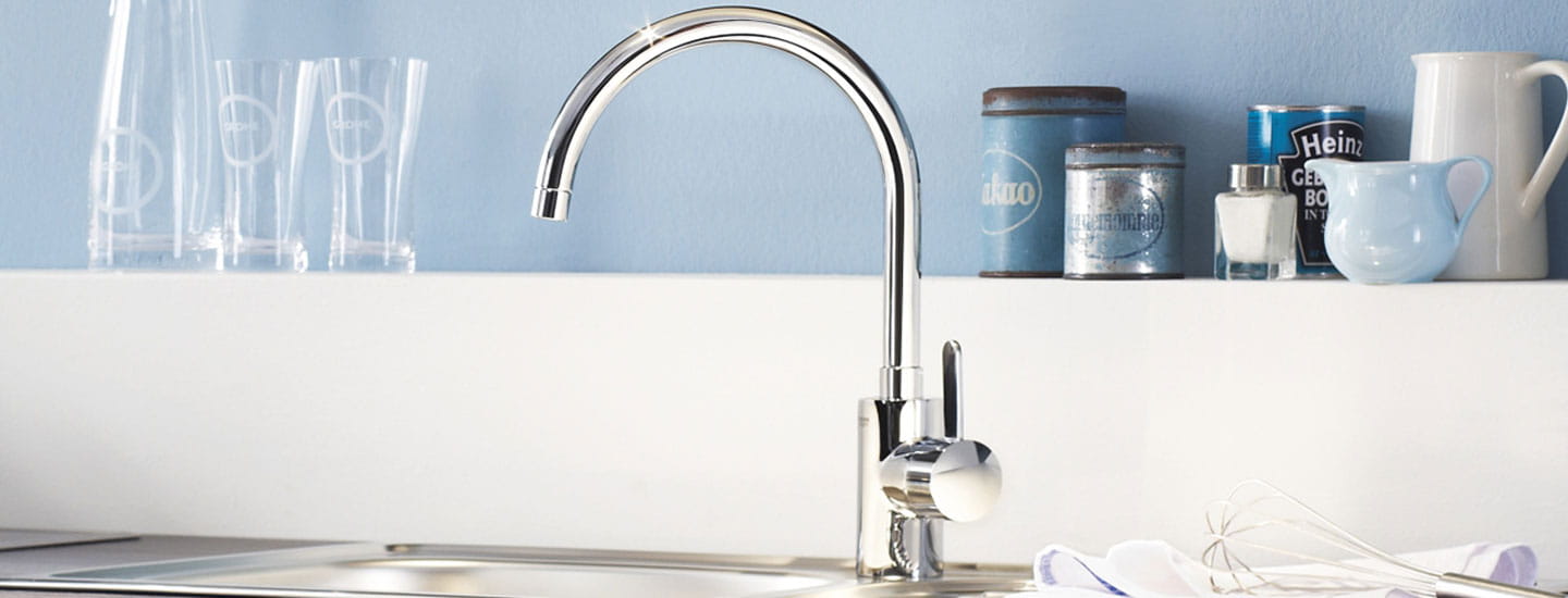 shiny kitchen faucet with glasses and containers on ledge behind