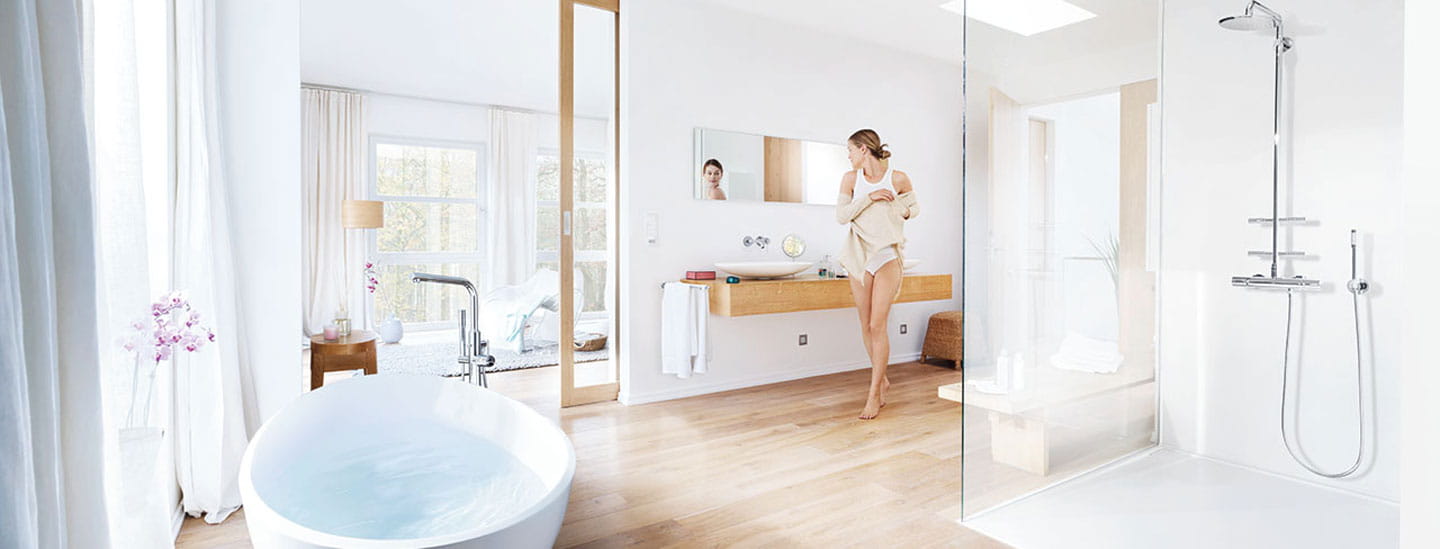 open bathroom with filled bathtub and woman looking in mirror