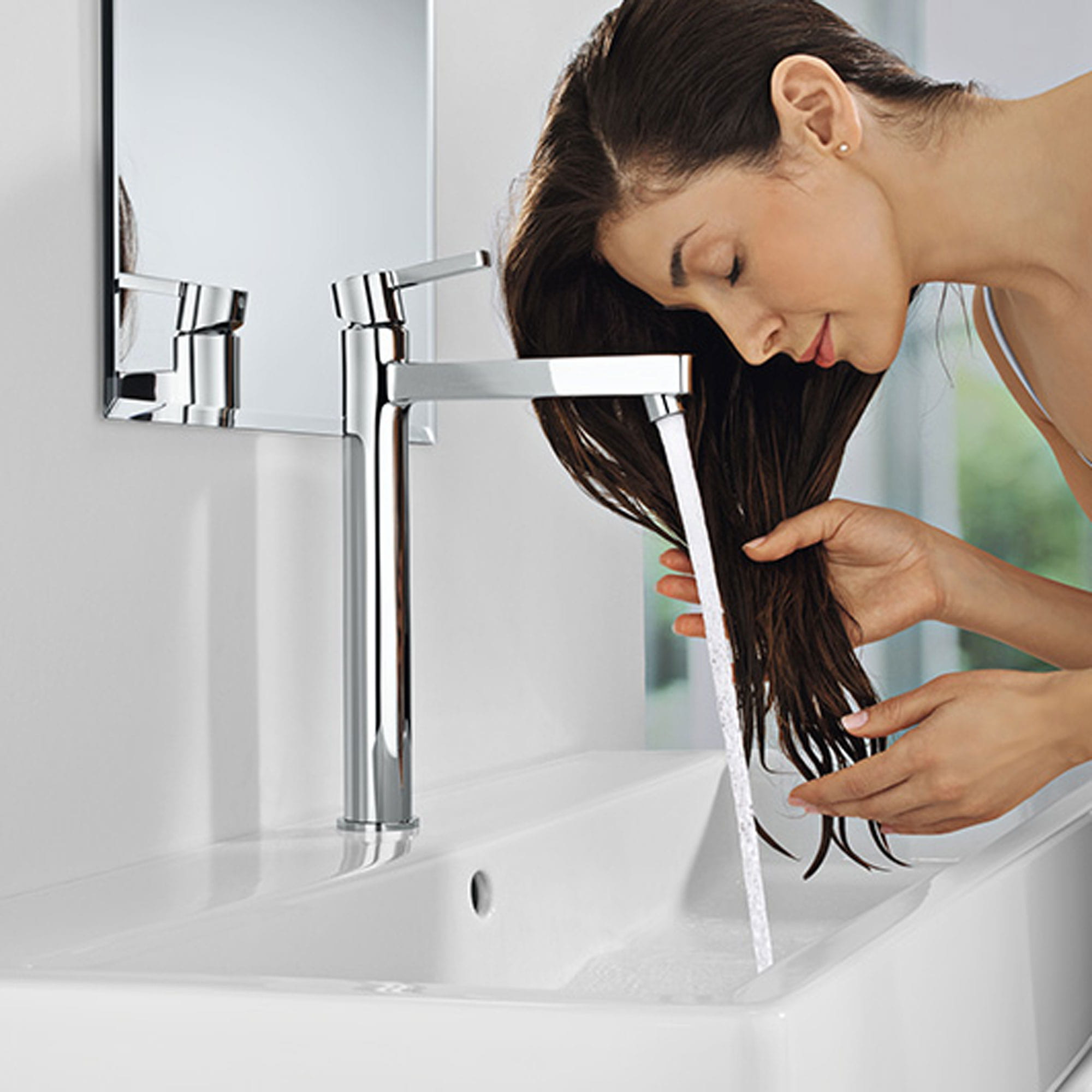 Une femme se lavant les cheveux sous un robinet grohe.