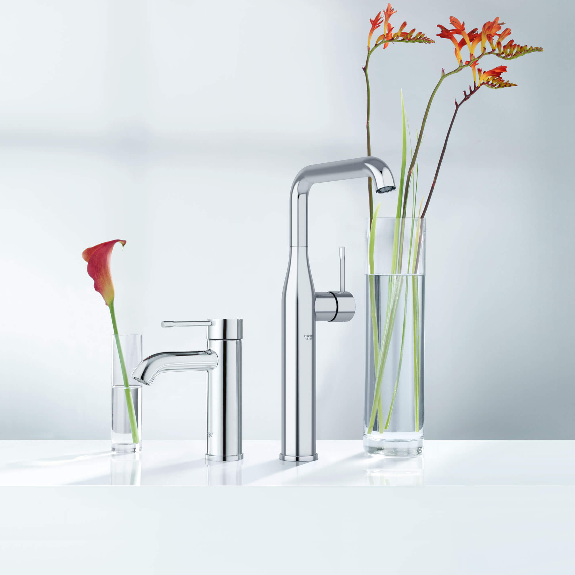 A pair of Grohe faucets next to vases filled with flowers.