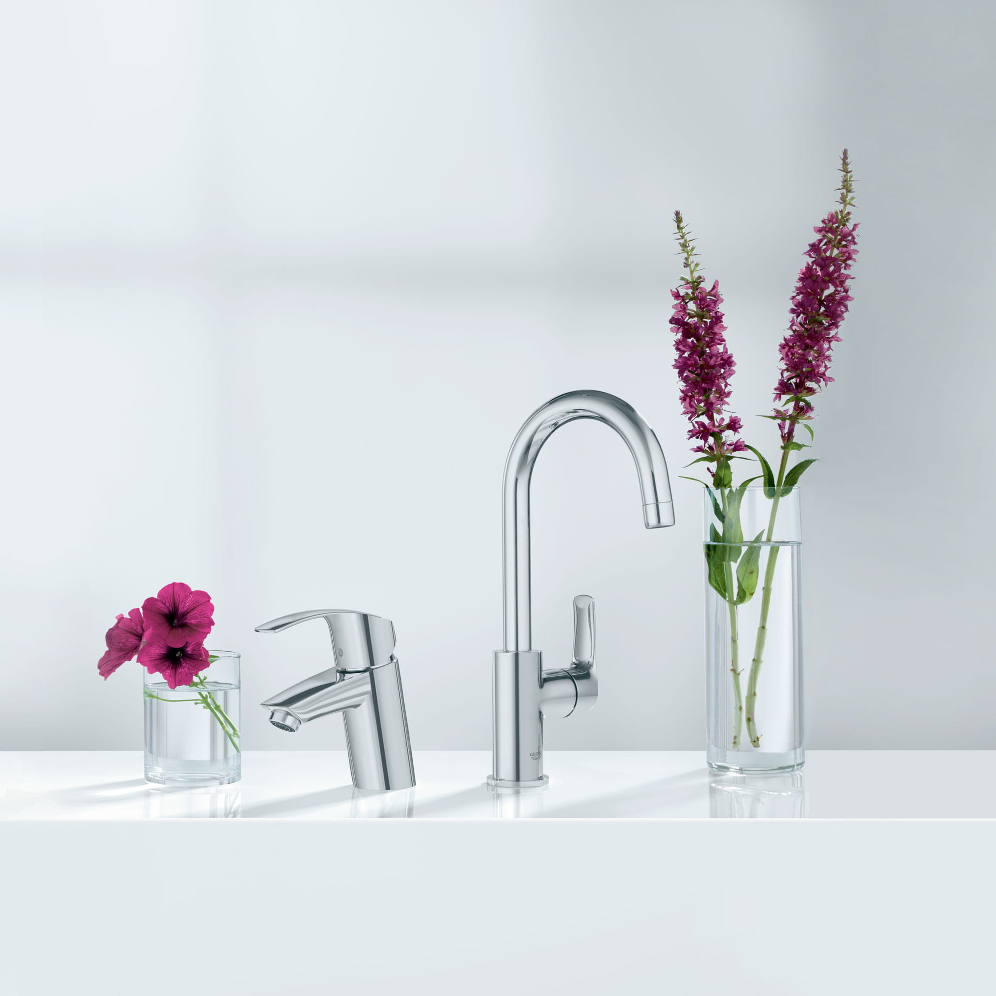 A pair of Grohe faucets next to vases filled with flowers.
